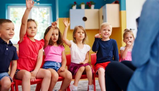 Children with hands up in a school room 
