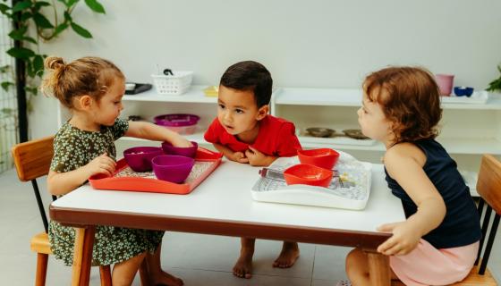 Three children sitting at a table eating snacks 