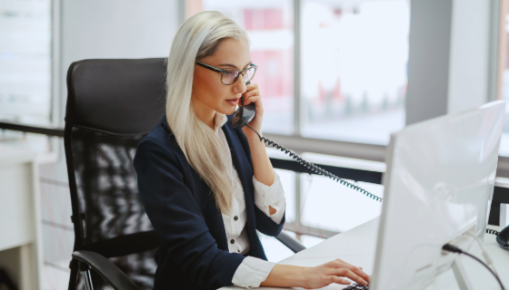 woman sitting at desk on the phone while simultaneously typing