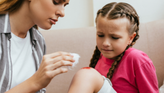 Woman applying first aid to a graze on a girl's knee