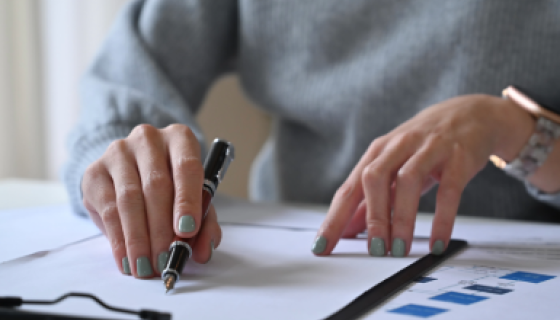 Hands with a pen looking up information on a papered clipboard.