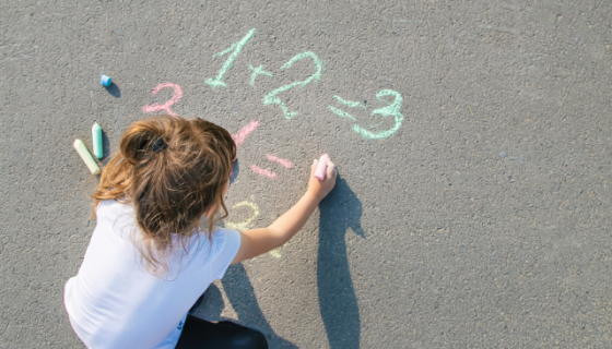 A little girl doing basic maths sums in multi-coloured chalk on cement