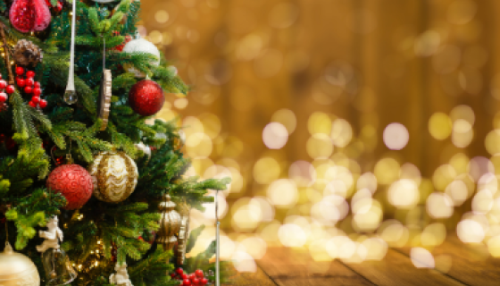 decorated christmas tree on left with blurred yellow christmas lights in the background