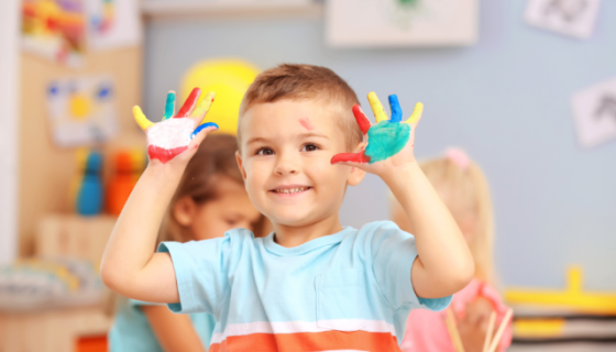 young boy looking at camera showing different coloured paints on hands