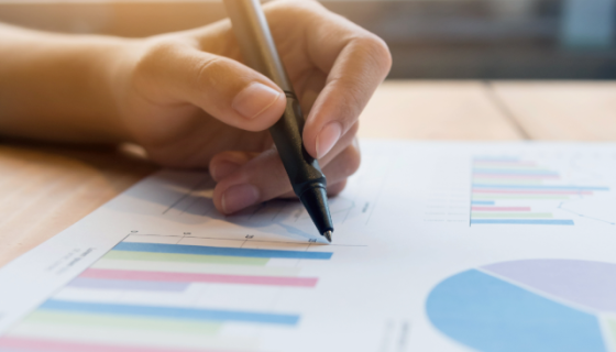 A hand holding a pen over a page of coloured graphs.