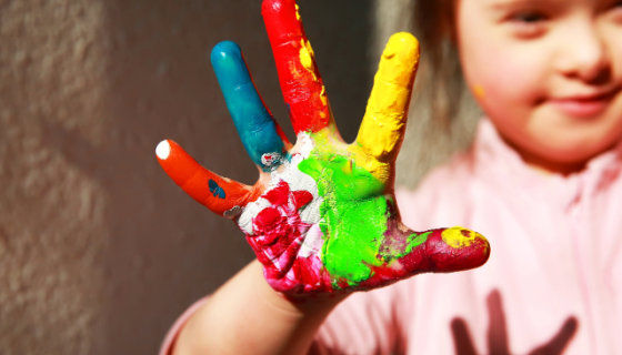 a girl holding up her open hand which has been painted in different colours