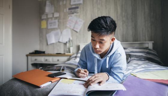 Male international student studying on his bed in a boarding room.