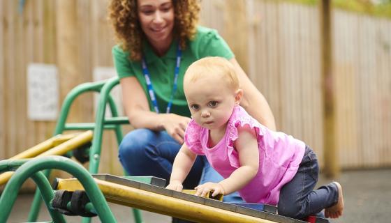 Baby crawling on play equipment with female educator supporting