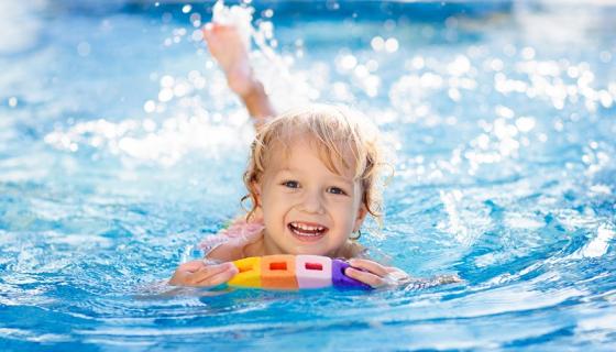 Three-year-old boy splashing in a swimming pool and using a colourful float board.