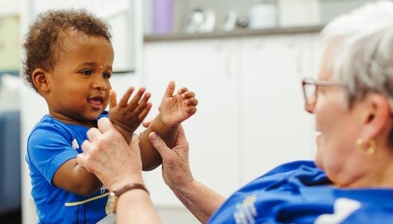 Educator with toddler on her lap holding his arms to help him clap