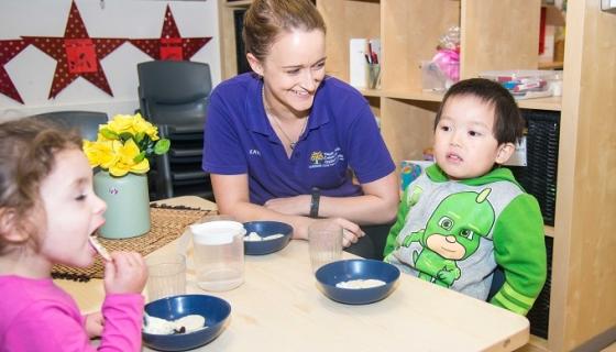 Female educator and two children who are eating at a table