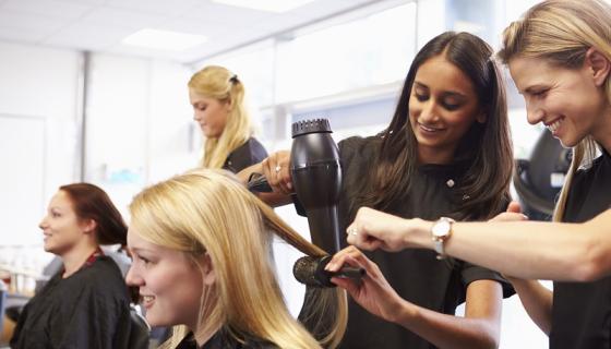 Female student assists with drying a client&#039;s hair in a hair salon